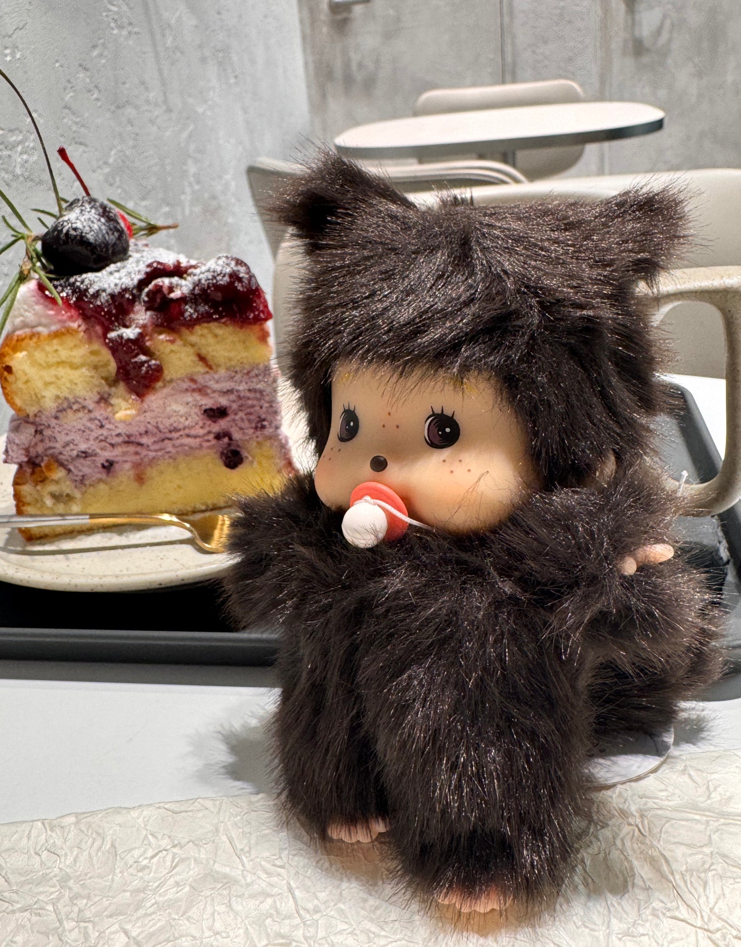 Plush doll keychain with bear-like ears placed next to a dessert, in a cozy, softly lit café environment.