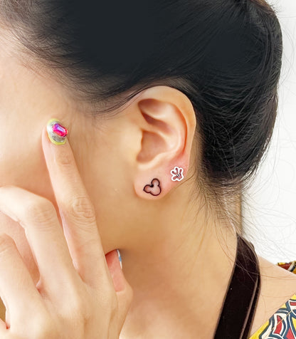 Playful styling with black Mickey silhouette and white glove earrings worn together, paired with colorful nail art and tied hair.
