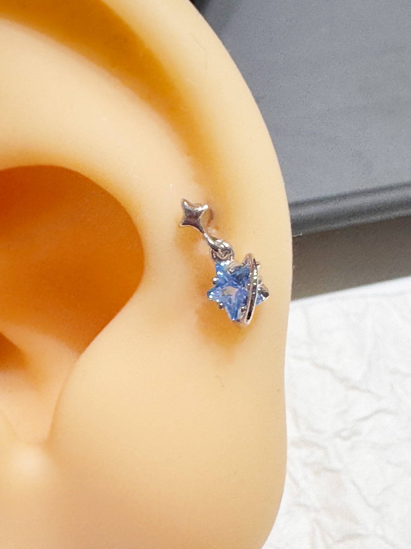 Silver planet and star piercing with blue cubic zirconia shown on a display ear model.
