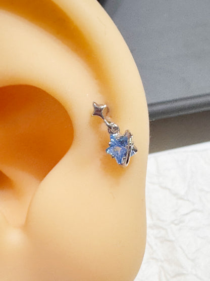 Silver planet and star piercing with blue cubic zirconia shown on a display ear model.