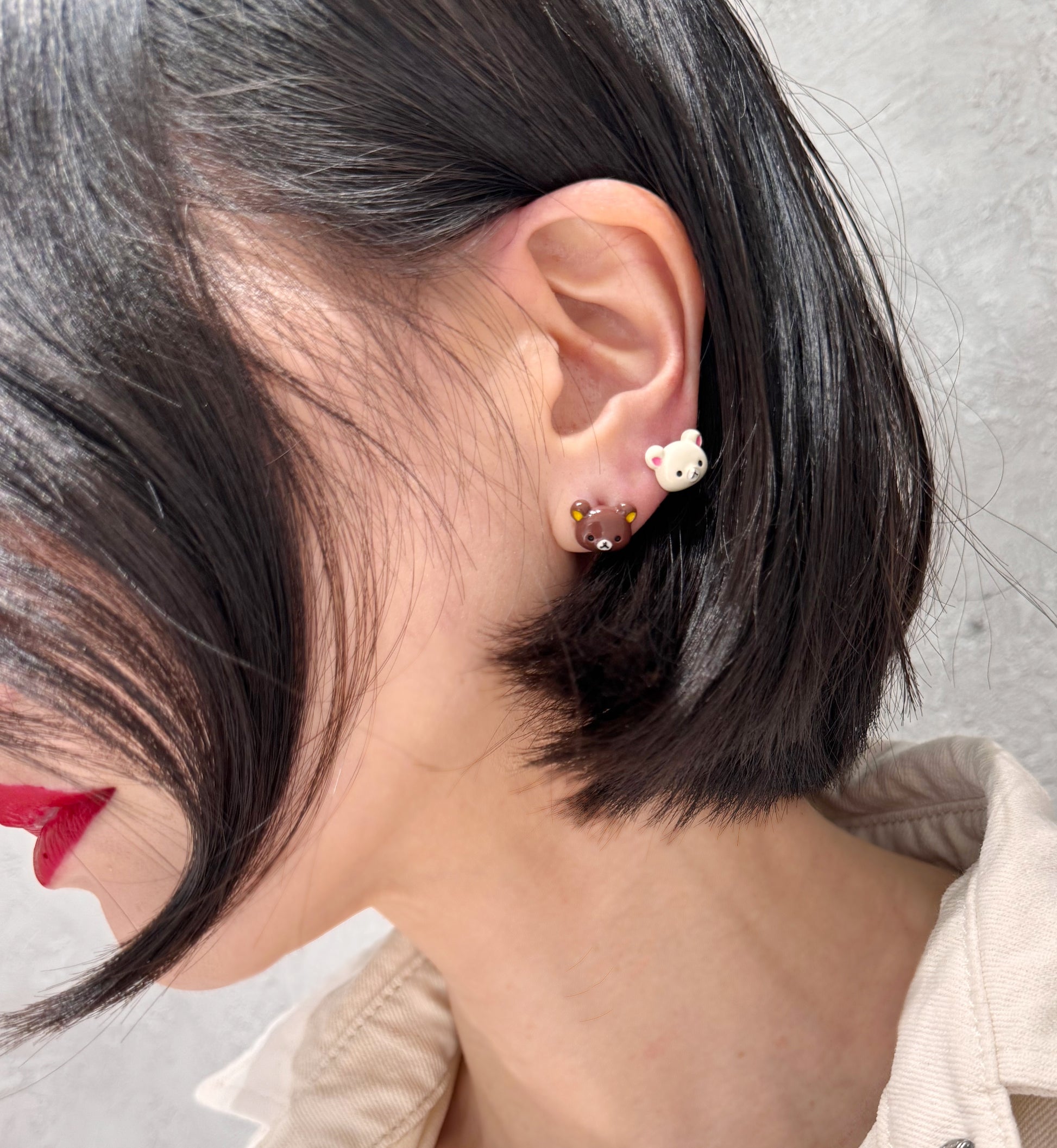 Person wearing mismatched brown and ivory bear-head stud earrings on the lower earlobe. Cute, playful handmade Korean earrings