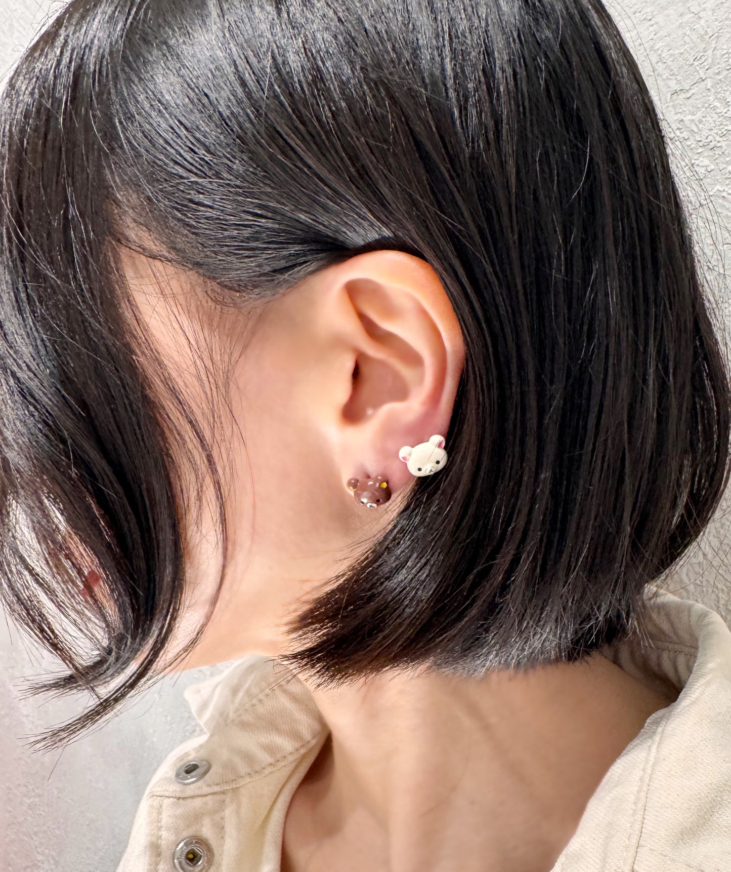 Side view of a person wearing tiny bear-head studs in brown and ivory, styled as mismatched earrings