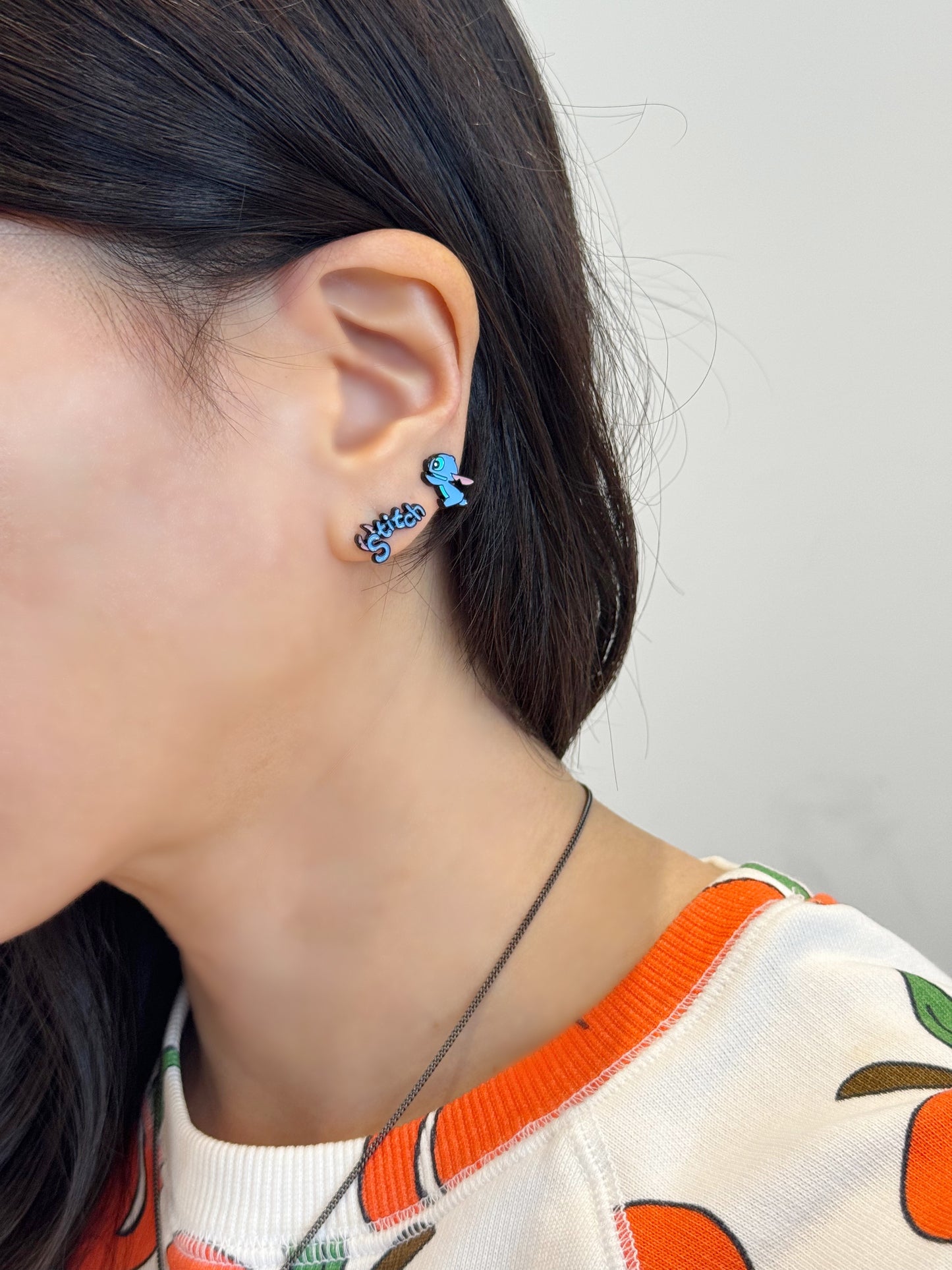 Walking Stitch and logo earrings styled on ear, minimal styling with orange fruit print sweater.