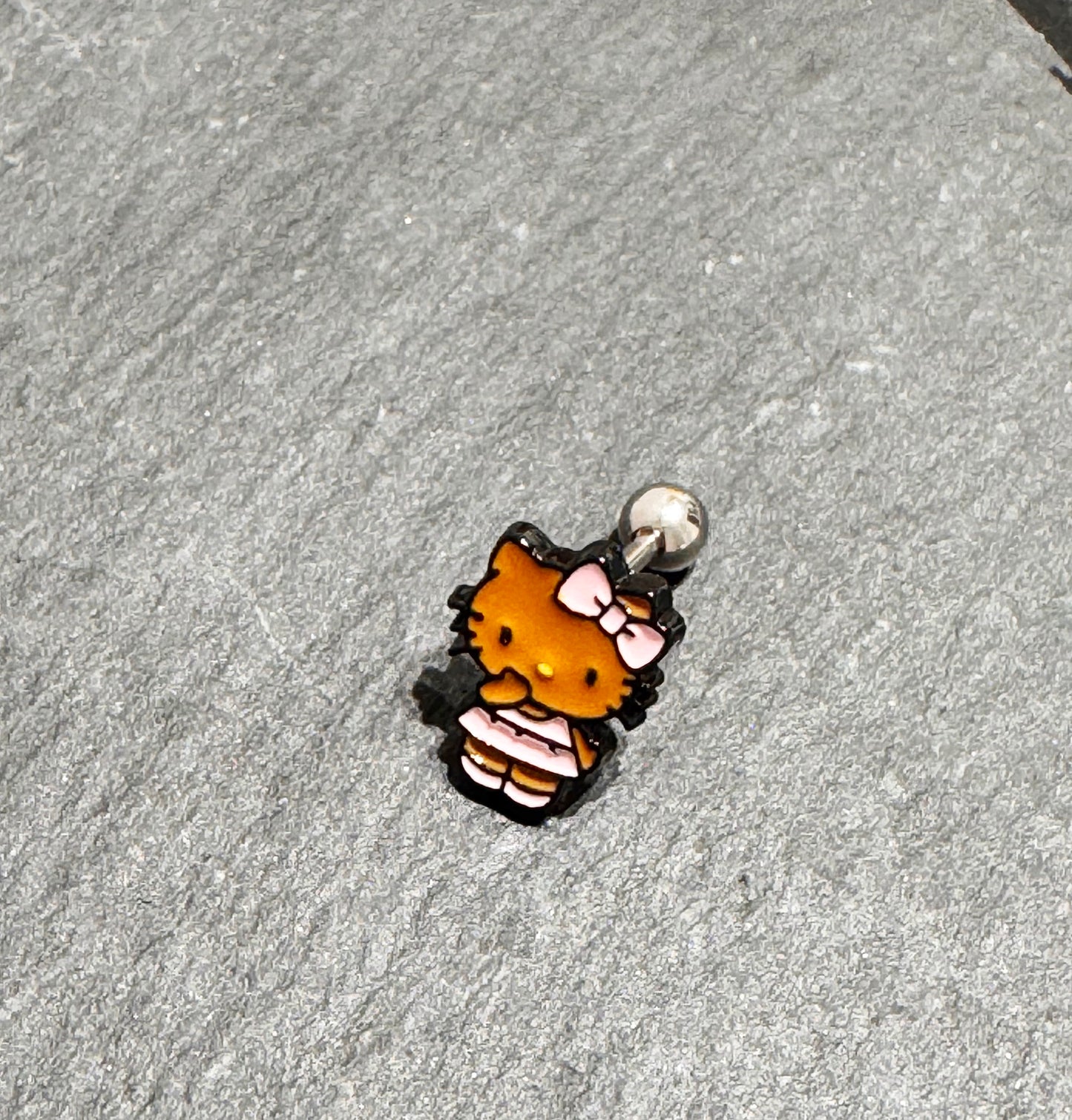 Adorable Hello Kitty–inspired piercing featuring a playful Hawaii-style cat in pink or red dress. Made with hypoallergenic surgical steel. Sold as single.