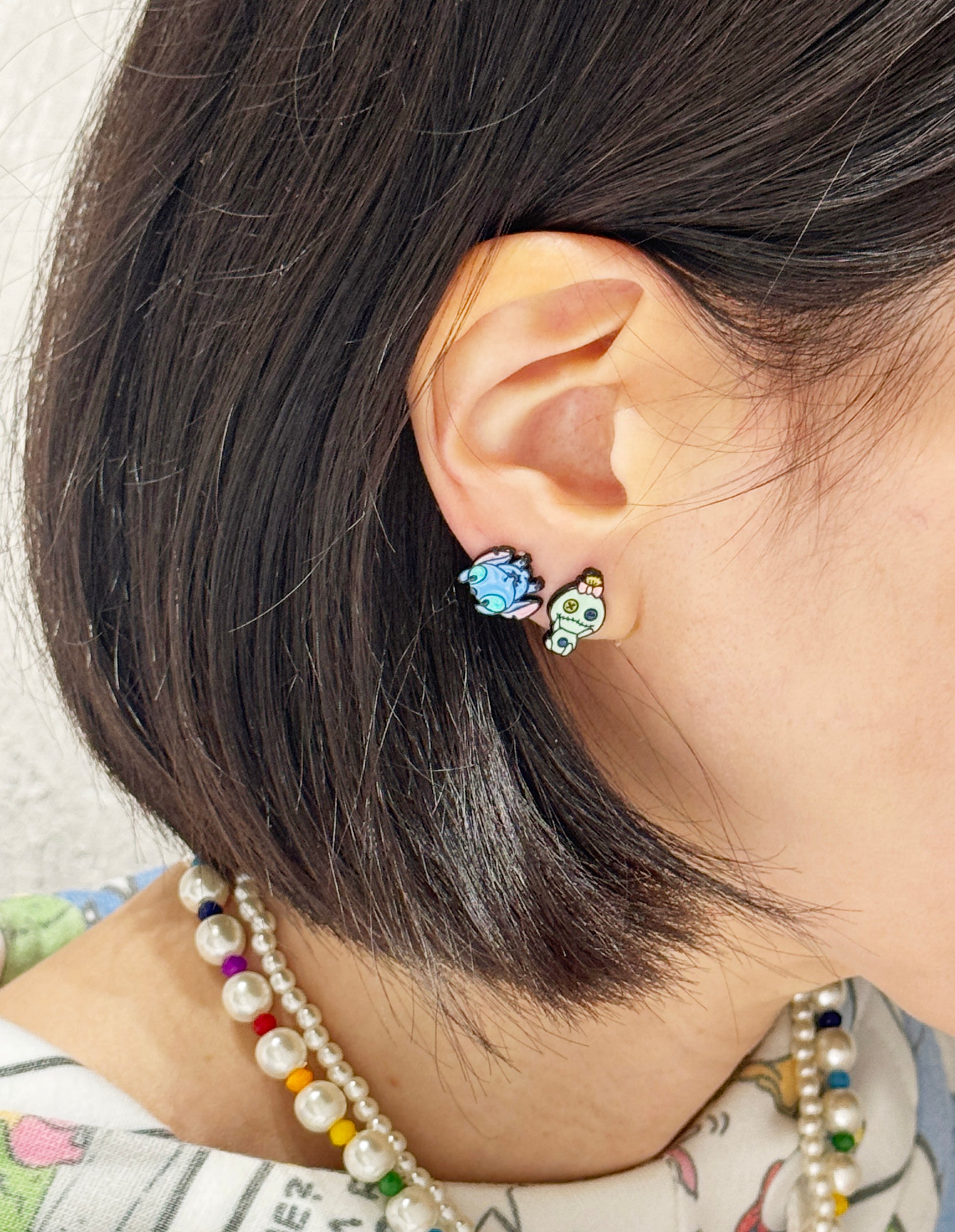 Stitch and Scrump earrings worn on ear with pearl necklace, pastel character styling