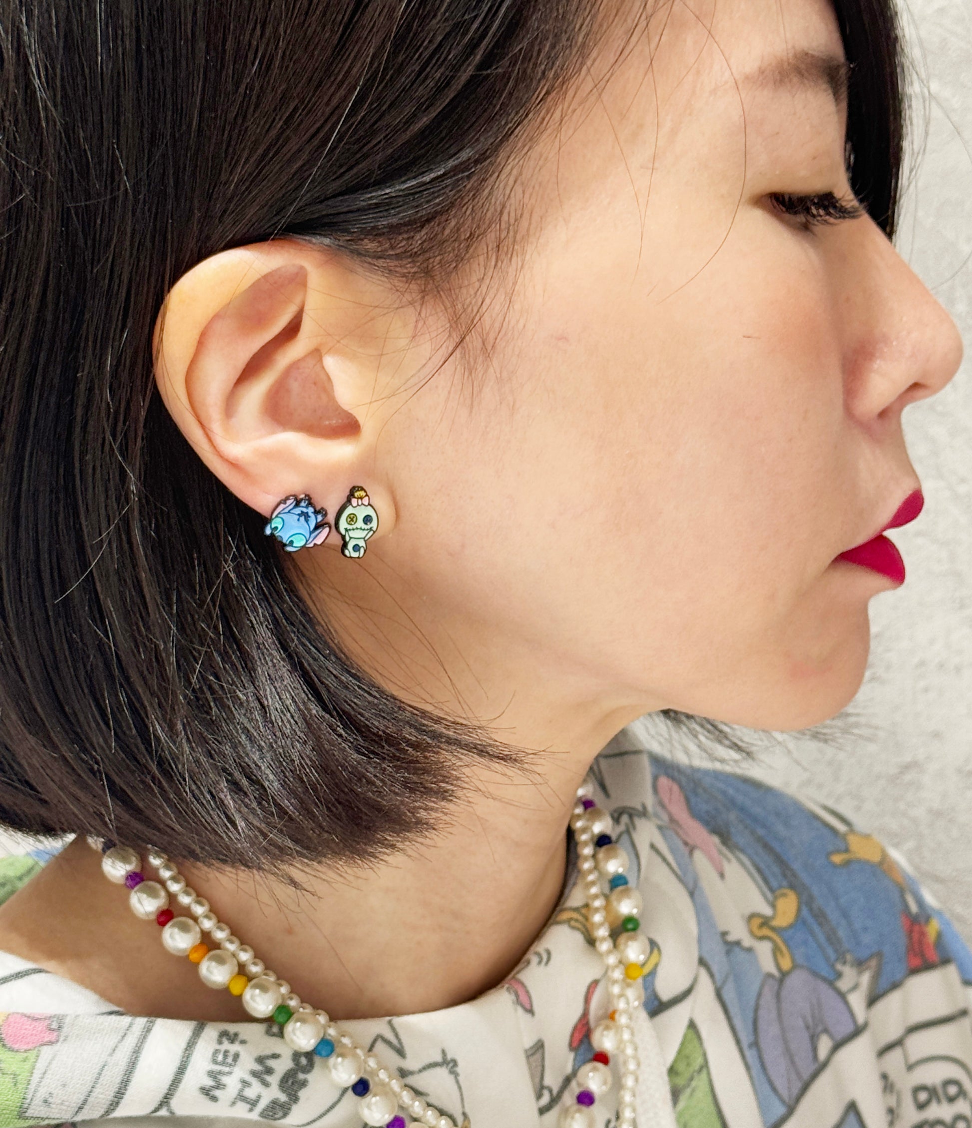 Stitch and Scrump earrings worn on ear with pearl necklace, pastel character styling