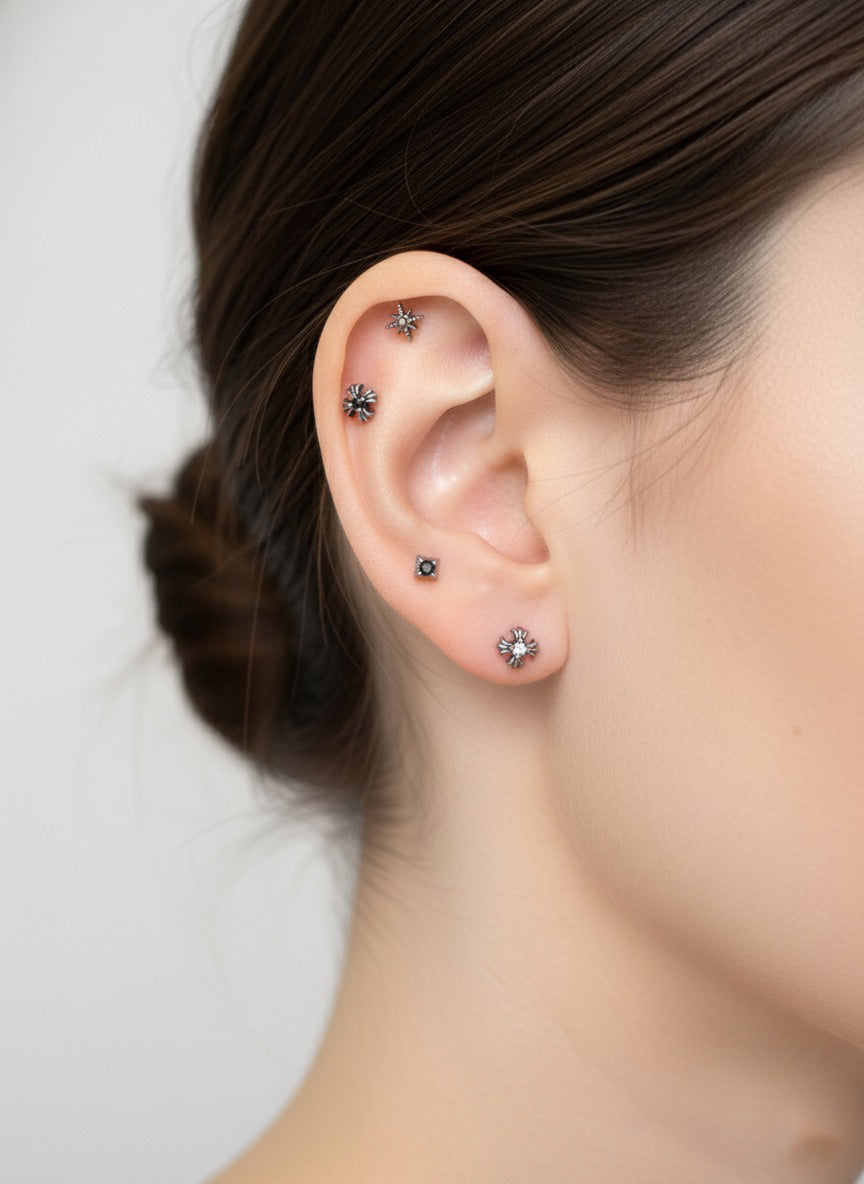 Full ear styling featuring five silver star and burst piercings in various positions—upper helix, mid-helix, and multiple lobes. A complete curated stack with dark crystal accents.