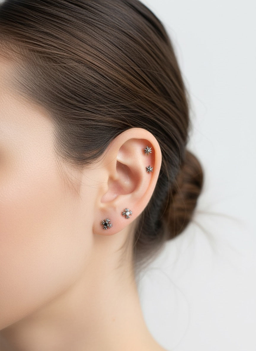 Full ear styling featuring five silver star and burst piercings in various positions—upper helix, mid-helix, and multiple lobes. A complete curated stack with dark crystal accents.