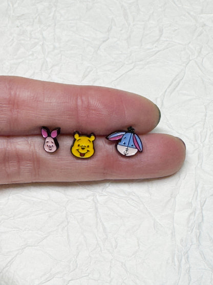 Three tiny barbell piercings (Piglet, Pooh, Eeyore) displayed across a person's fingers for size comparison.