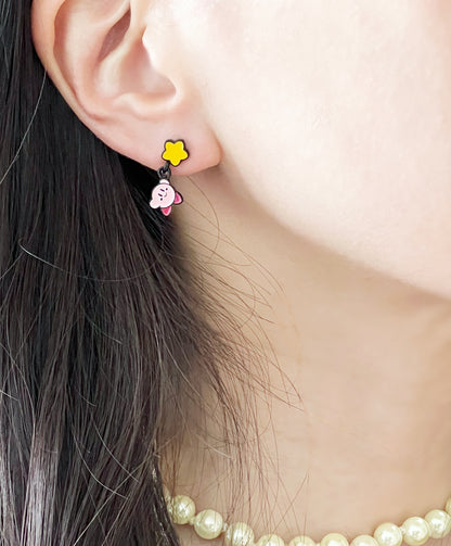 Close-up of a worn Kirby earring with a yellow star top and dangling flying Kirby charm on the earlobe.