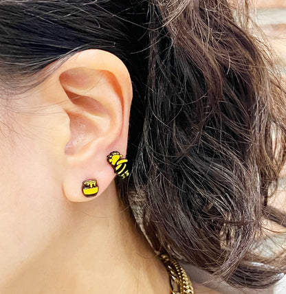 Close-up of ear wearing honey pot and Pooh character earrings together, with curly hair and casual styling.