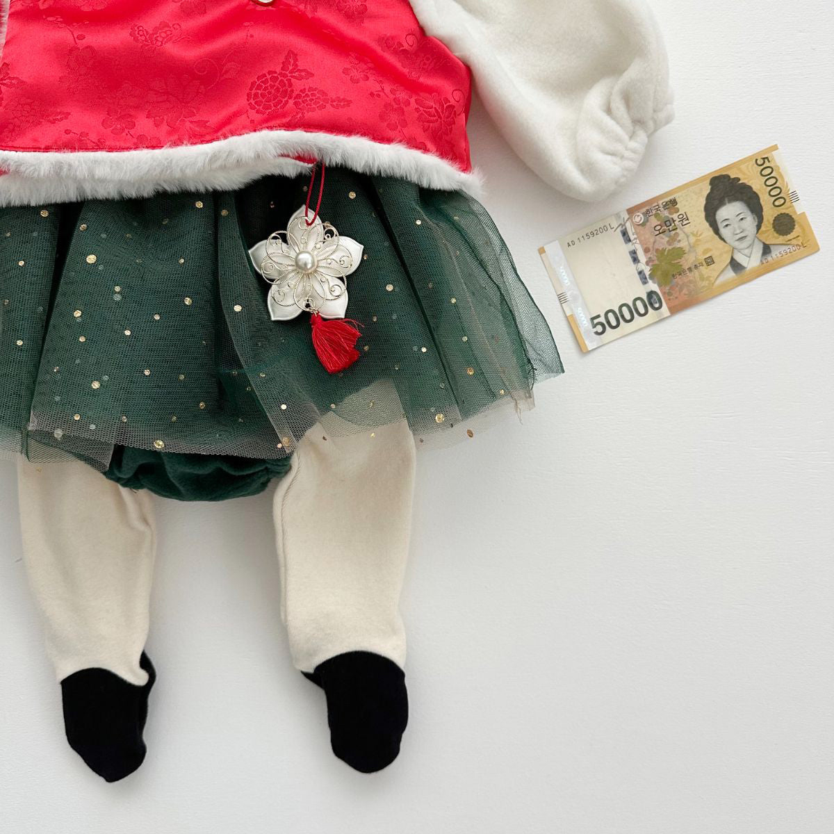 Korean traditional norigae ornament with red tassel on Santa-style hanbok outfit, shown with Korean 50,000 won bill for size reference
