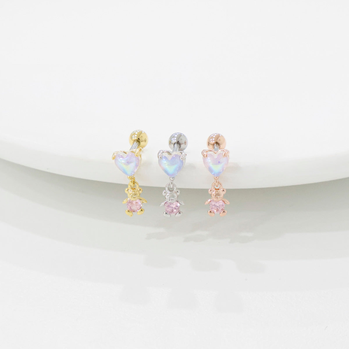 Three heart-shaped and bear earrings in gold, silver, and rose gold on a white background