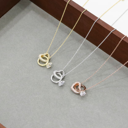 Three interlocking heart ring necklaces displayed on gray stone