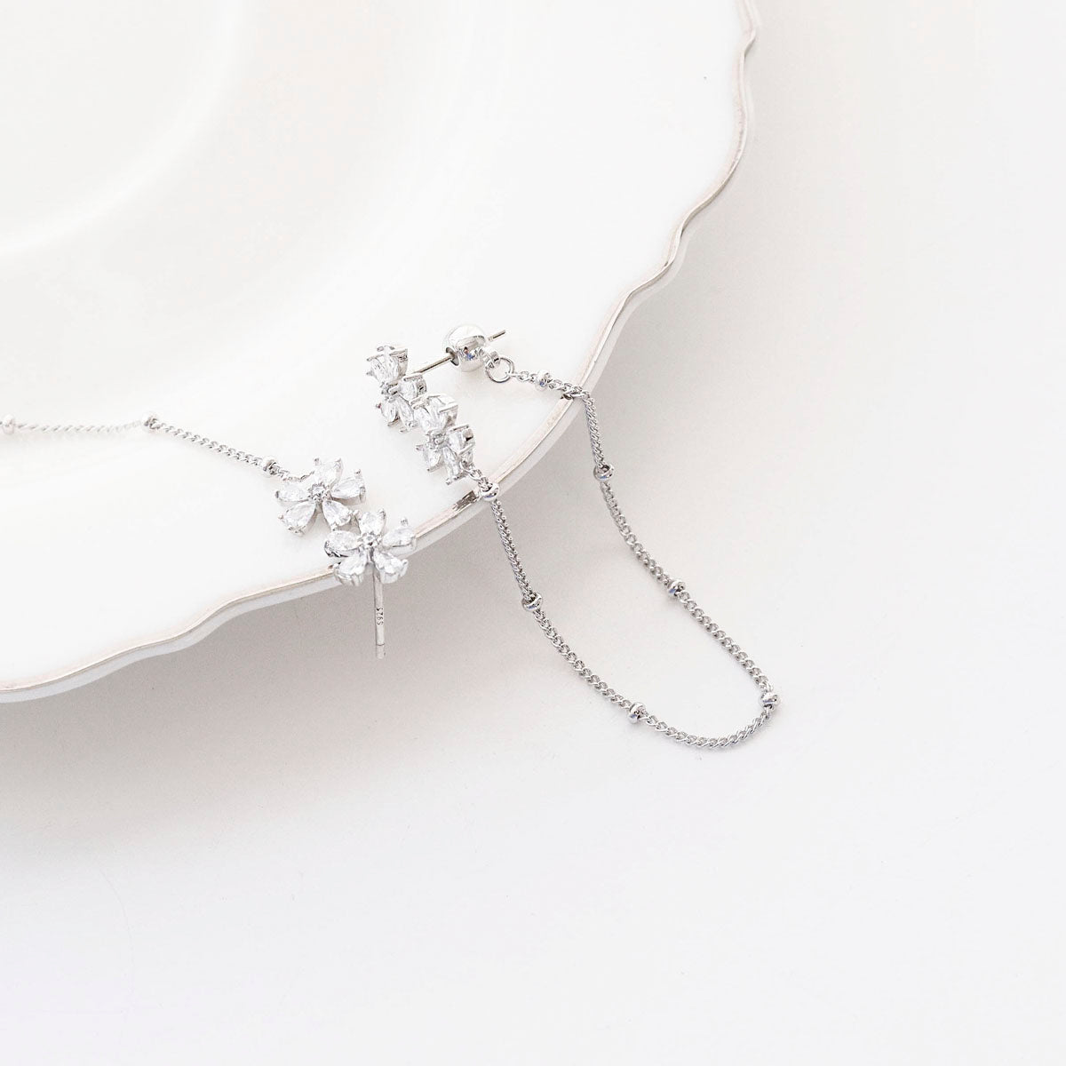 Flat lay of silver two-way floral crystal chain earrings on white background