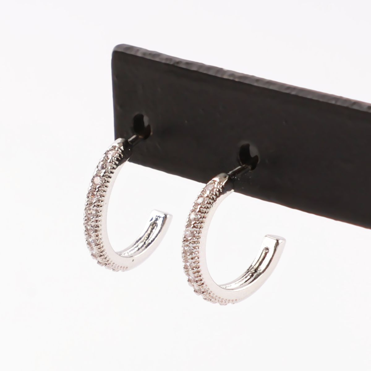 Close-up of silver half hoop earrings with pavé cubic zirconia detailing, displayed on a black card.