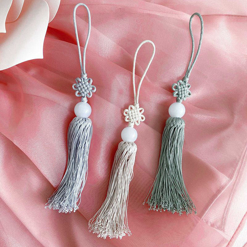 Three Korean norigae tassel charms with jade beads and traditional knots on pink silk background