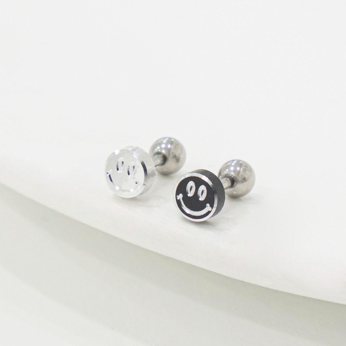 Silver and black smiley face stud earrings on white background