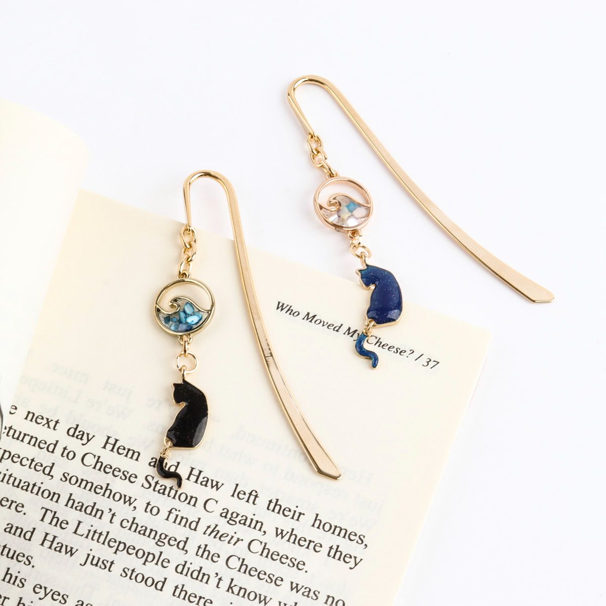 Close-up of gold cat bookmark with blue wave charm hanging outside book page, whimsical page marker detail