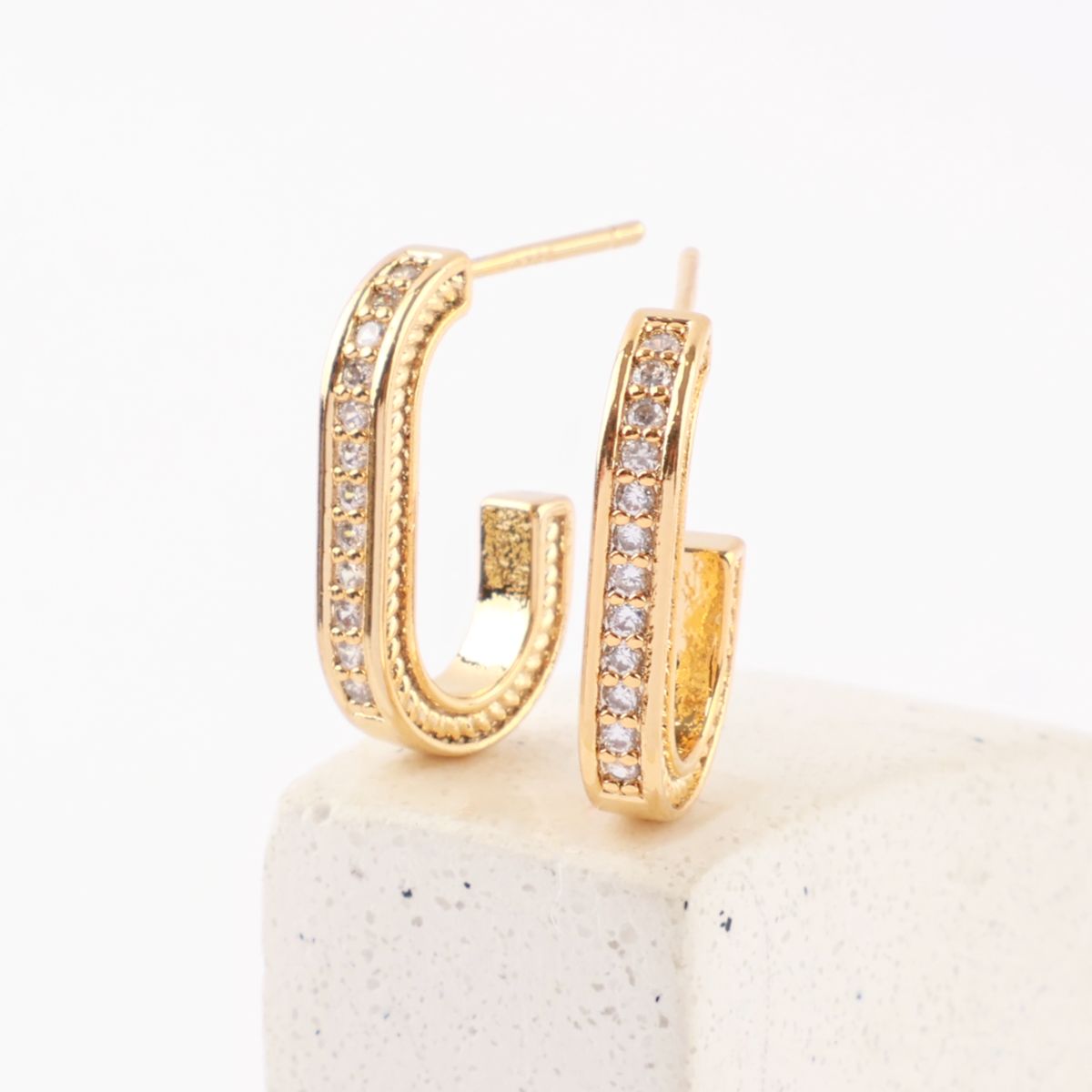 Gold oval drop stud earrings on white stone display