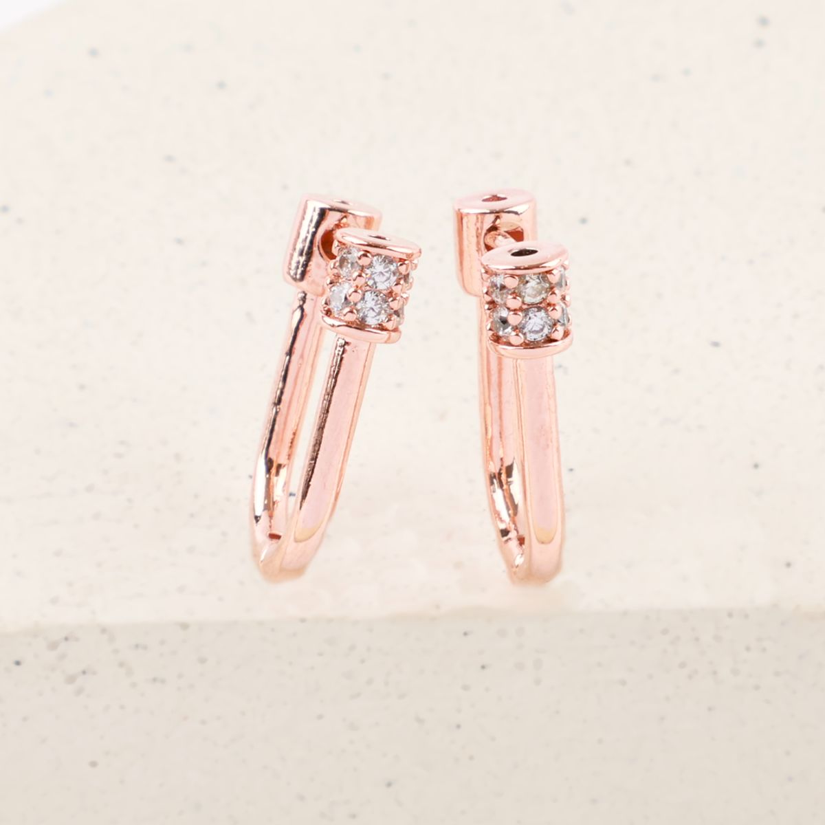 Close-up of rose gold hoop earrings with pavé crystal cylinder clasp on white stone background.