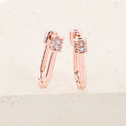 Close-up of rose gold hoop earrings with pavé crystal cylinder clasp on white stone background.