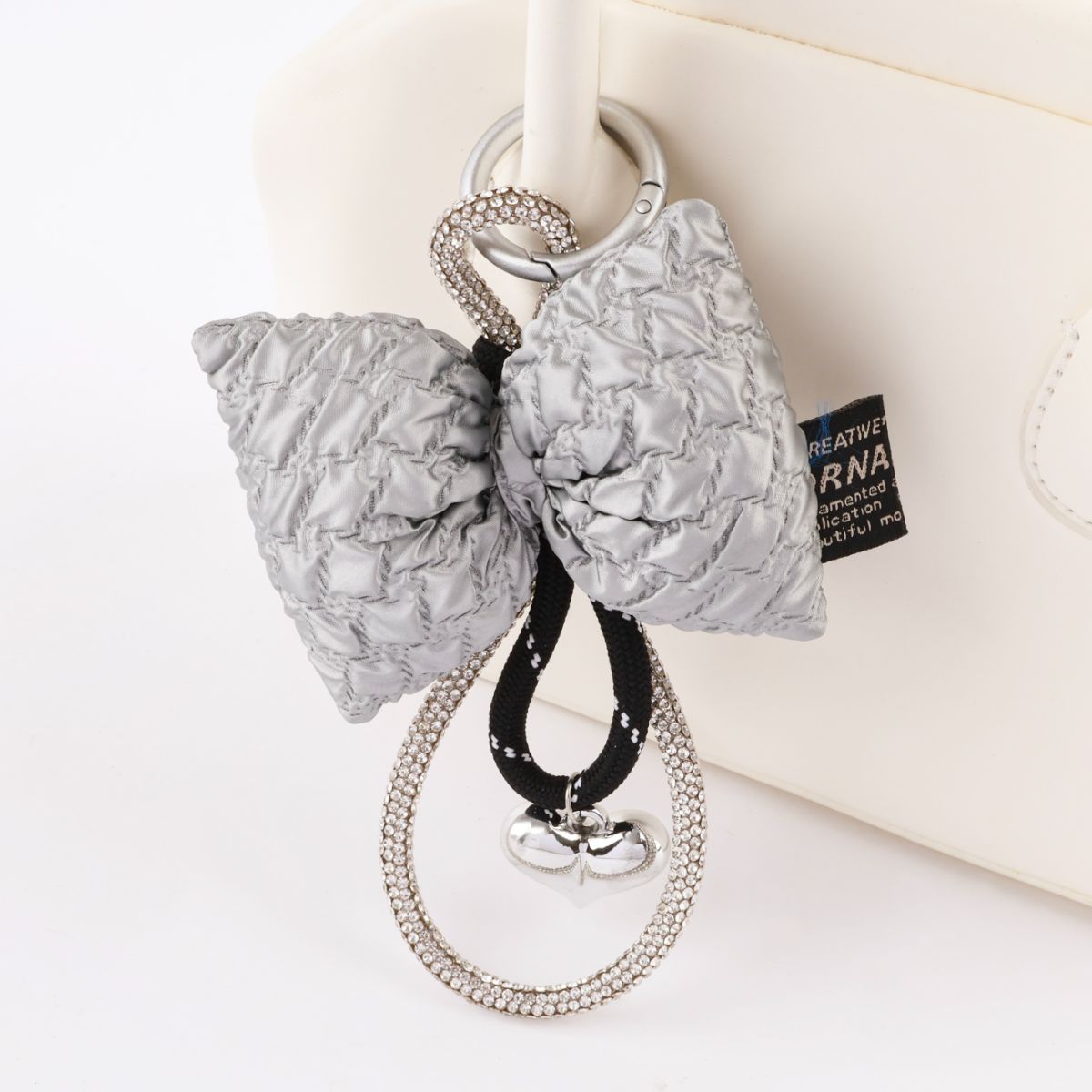 Close up of silver quilted bow keychain with rhinestone loop and heart charm detail