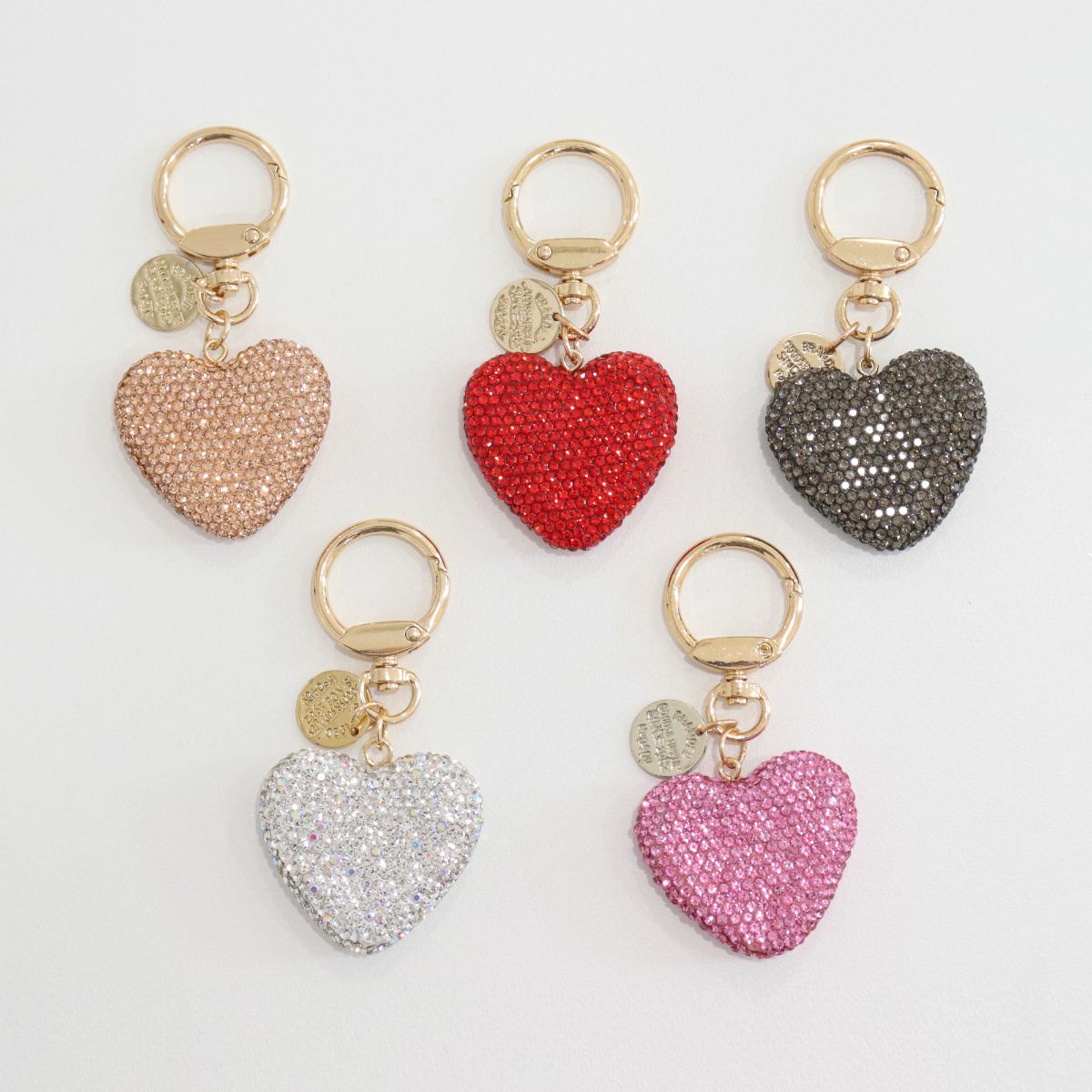 A set of 5 glittering heart keychains with gold keyrings and circular tags.
Colors: nude, red, black, white, and pink.
Displayed flat on a white background