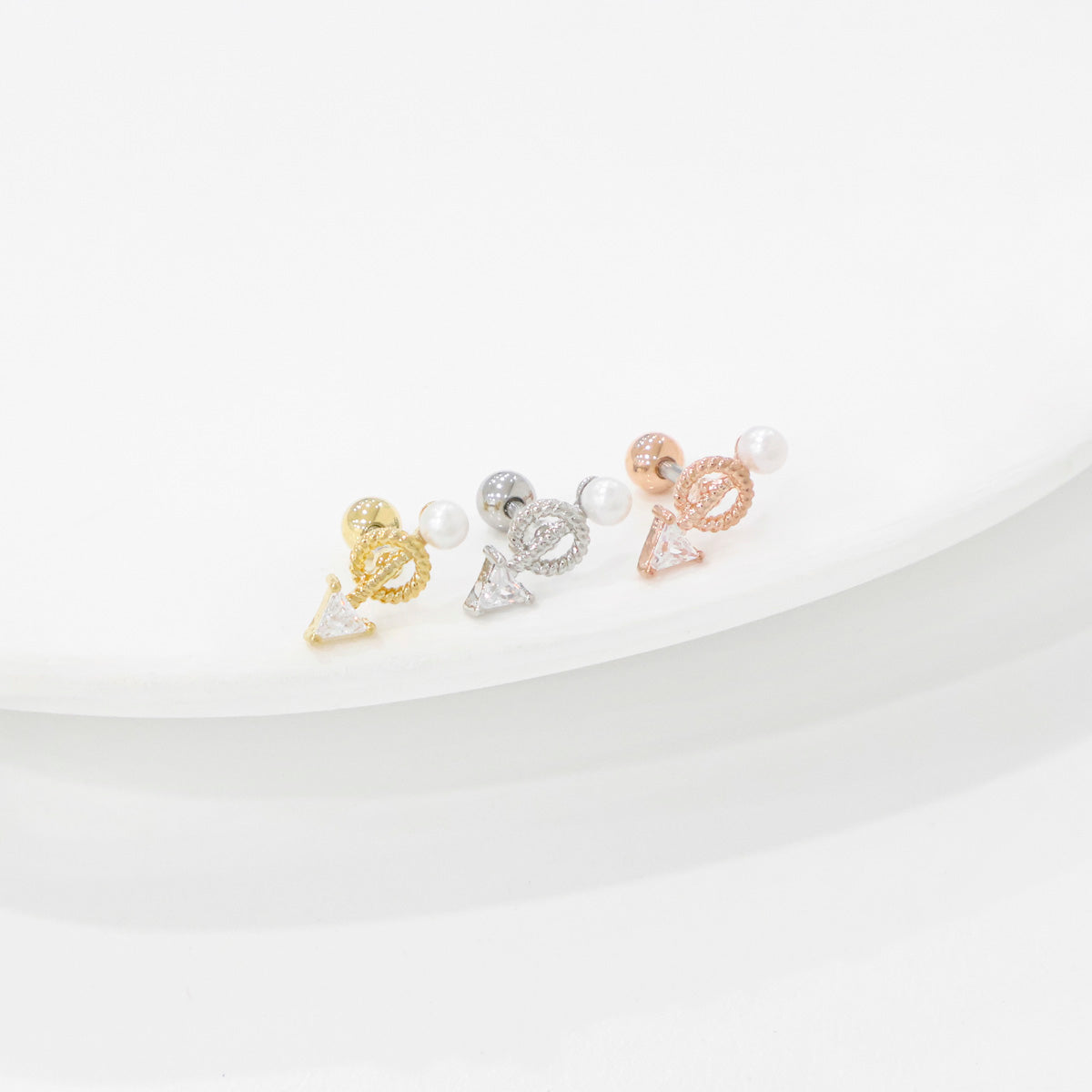 Flat lay of three colors: antique gold, ice silver, and romantic rose gold arrow helix barbell studs with pearl