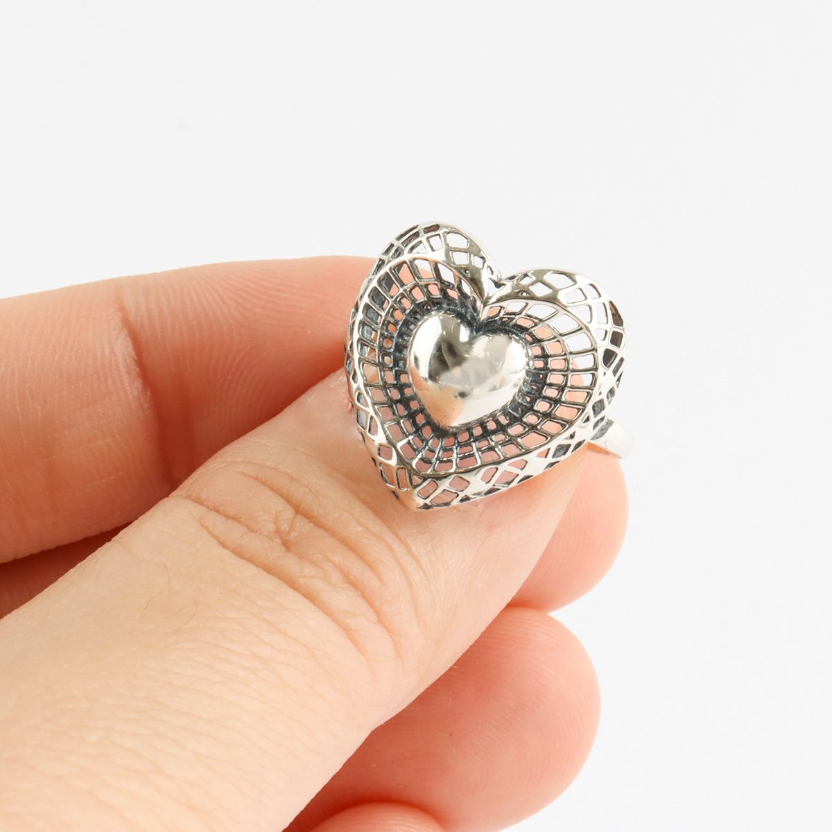 Hand holding vintage silver heart ring showing intricate 3D filigree lattice and polished center heart