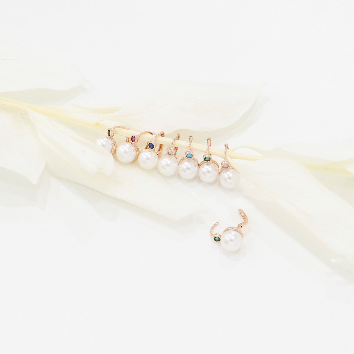 Assortment of colorful pearl drop earrings lined up on a white feather branch, showing 8 color options.