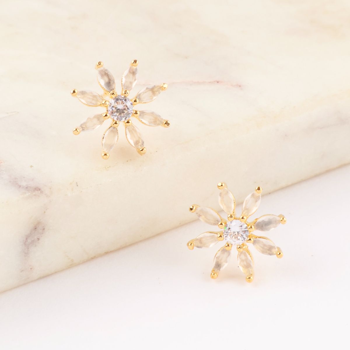 Gold-tone floral stud earrings with clear marquise stones and central cubic zirconia, placed on a marble surface.