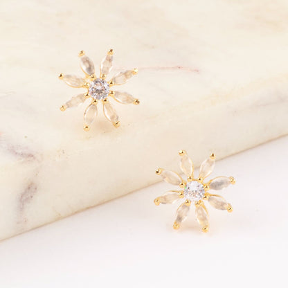 Gold-tone floral stud earrings with clear marquise stones and central cubic zirconia, placed on a marble surface.
