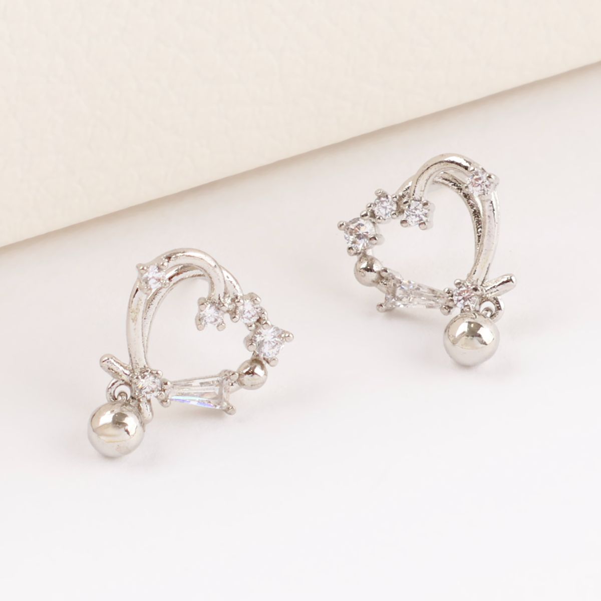 Silver heart drop earrings with cubic zirconia crystals and ball charm on beige surface, curved heart design with baguette stone, brass with 925 silver posts, handcrafted in South Korea