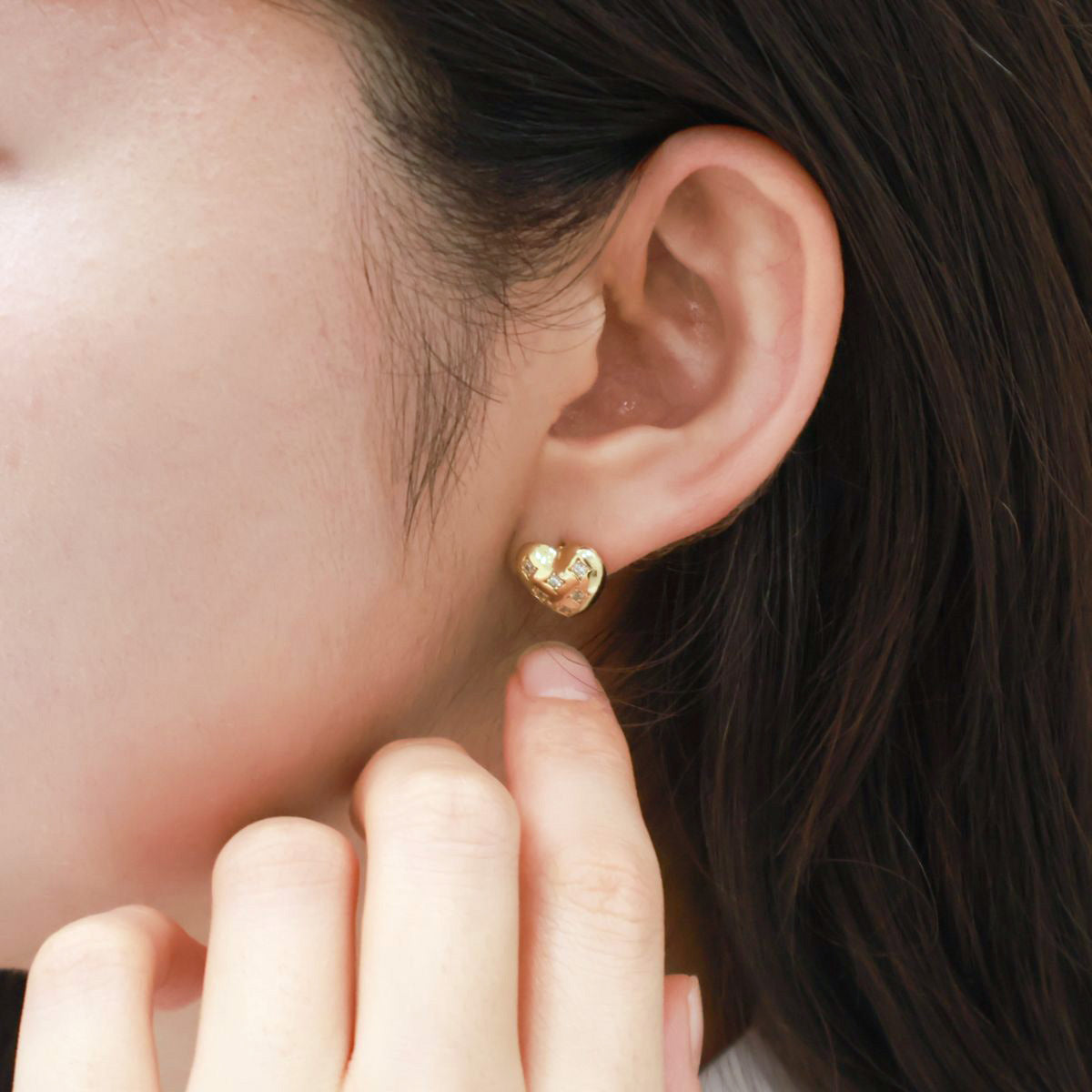 Side angle of gold heart stud earrings with designer-inspired quilted texture on ear