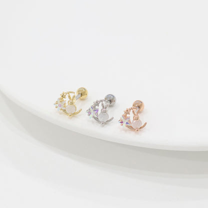 Three bunny moon barbell earrings viewed from a higher angle, showing gold, silver, and rose gold variants neatly lined up on a soft white surface.