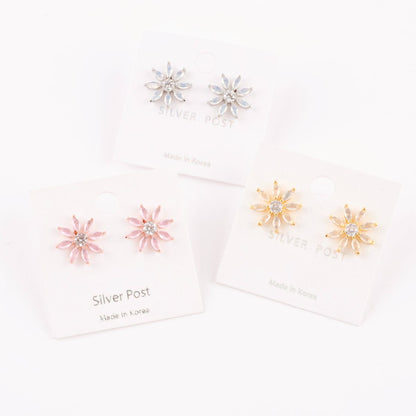 Set of three color variants of daisy-like earrings (gold, pink, and silver) arranged in front of their matching earring cards.