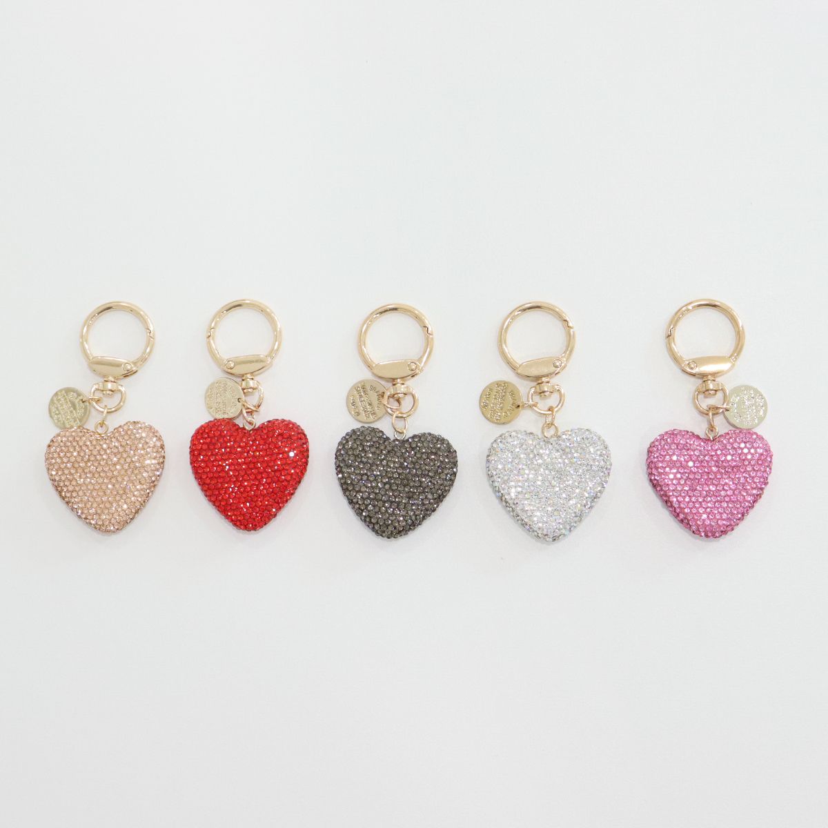 Top-down view of five rhinestone heart keychains arranged in a row.
Each has a gold keyring and a small gold medallion.