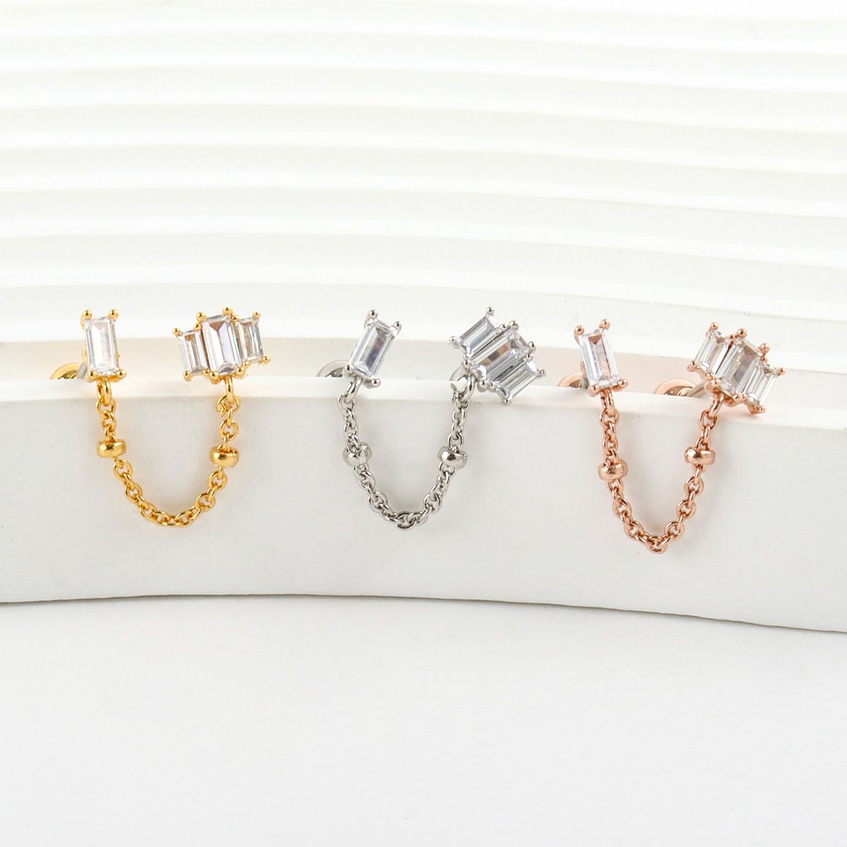 Three Baguette CZ Chain Double Stud Earrings in gold, silver, and rose gold colors lined side by side, showcasing their rectangular CZ stones and delicate chain links.