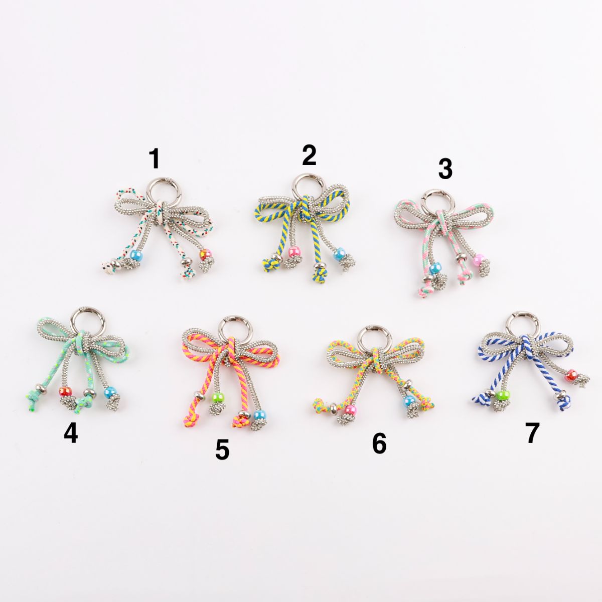Seven color options of handmade rhinestone rope bow bag charms laid flat display