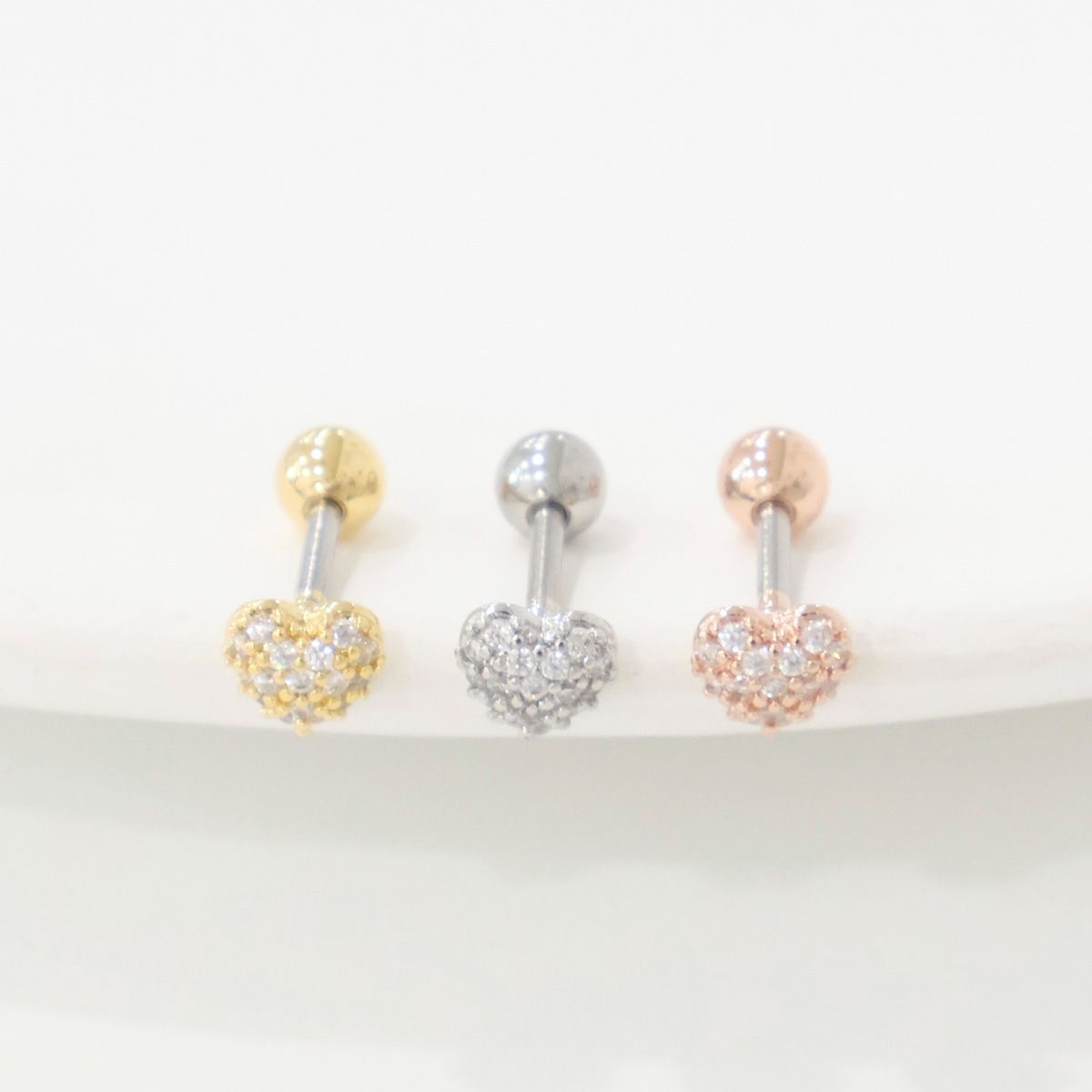 Gold, silver, and rose gold pavé heart earrings lined up on white surface, front-facing.