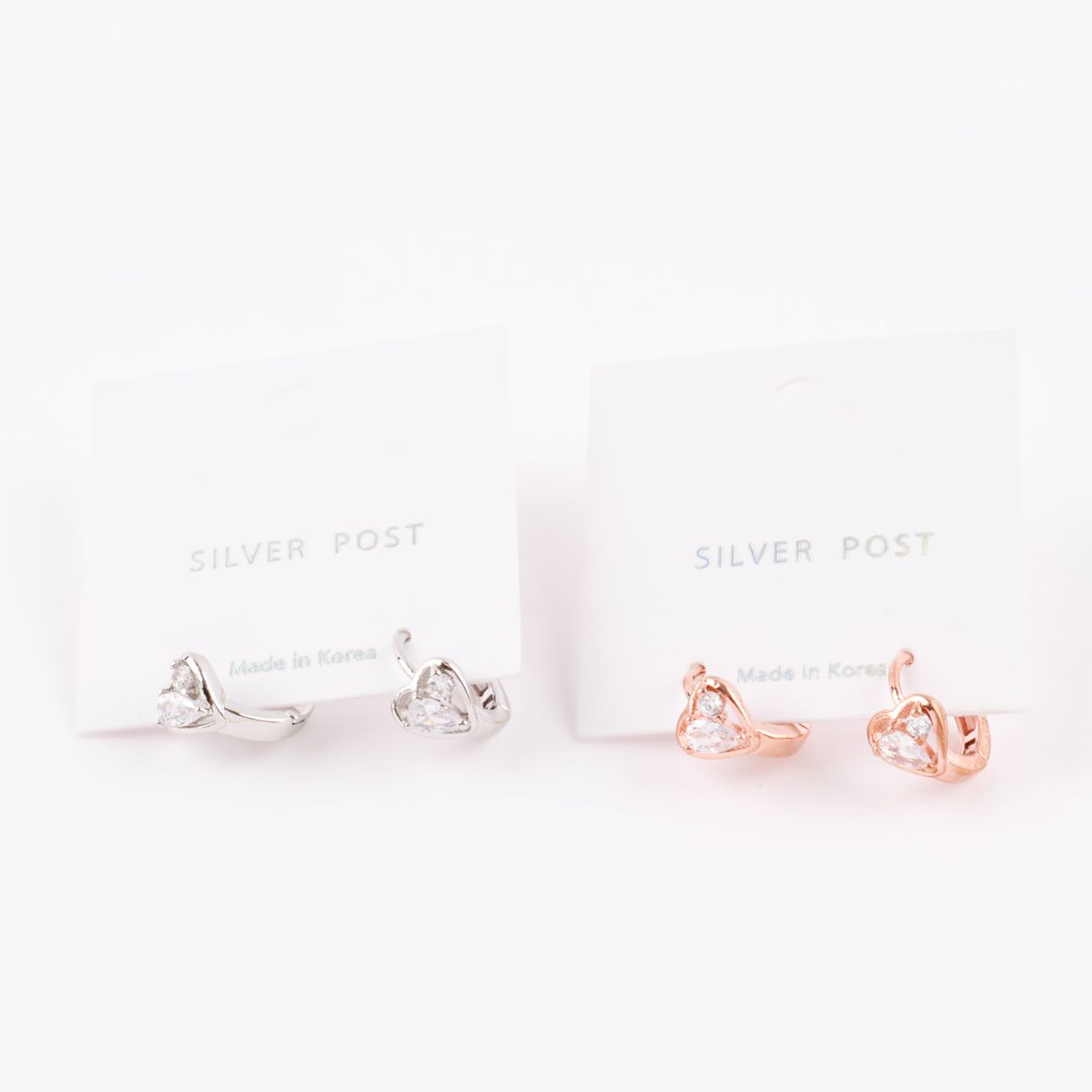 Rose gold and silver heart huggie earrings displayed on jewelry cards labeled "Silver Post" and "Made in Korea."