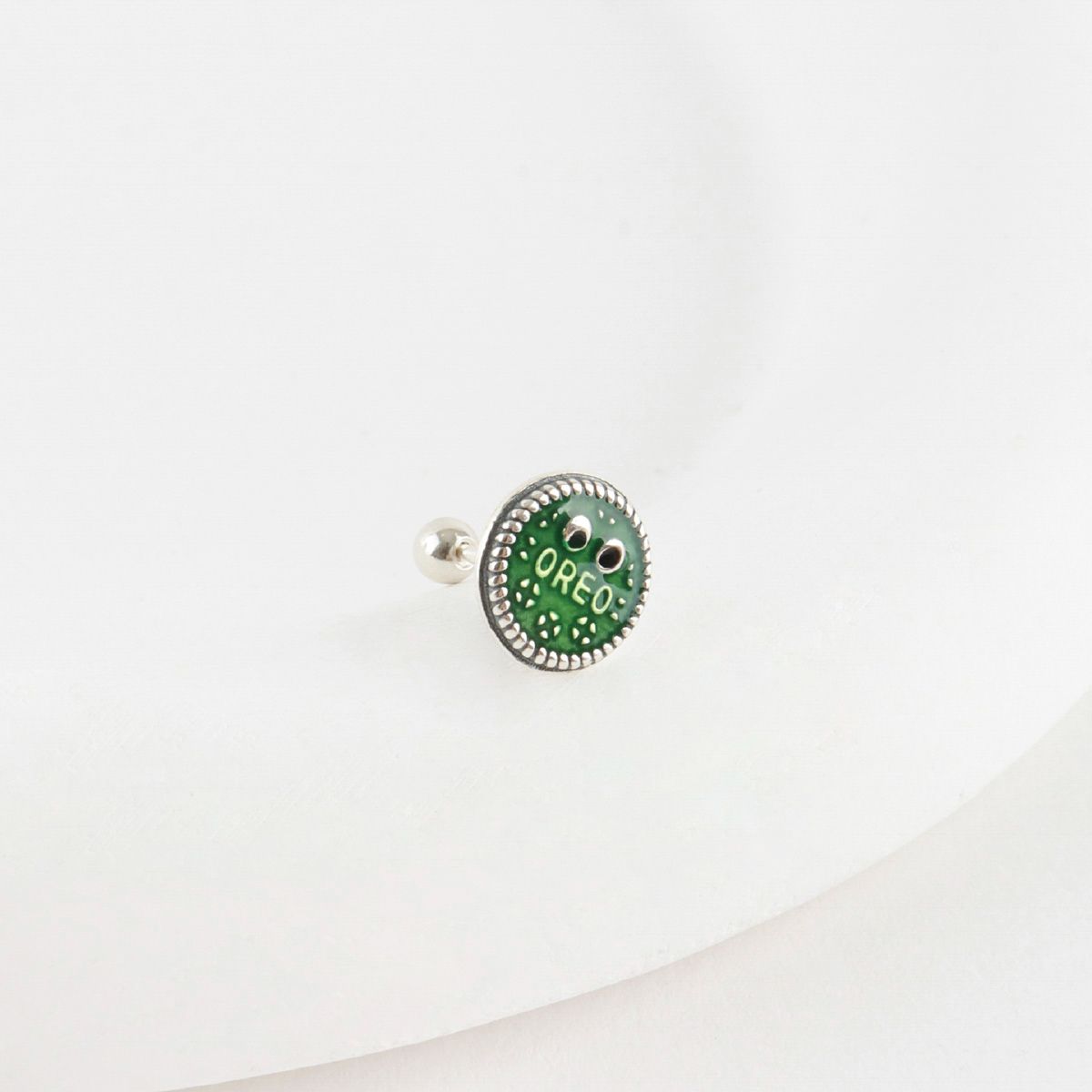 Close-up of green Oreo piercing on white background showing enamel detail and surgical steel body