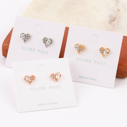 Heart-shaped silver post earrings in three color options displayed on minimal earring cards, with a marble and wood backdrop.