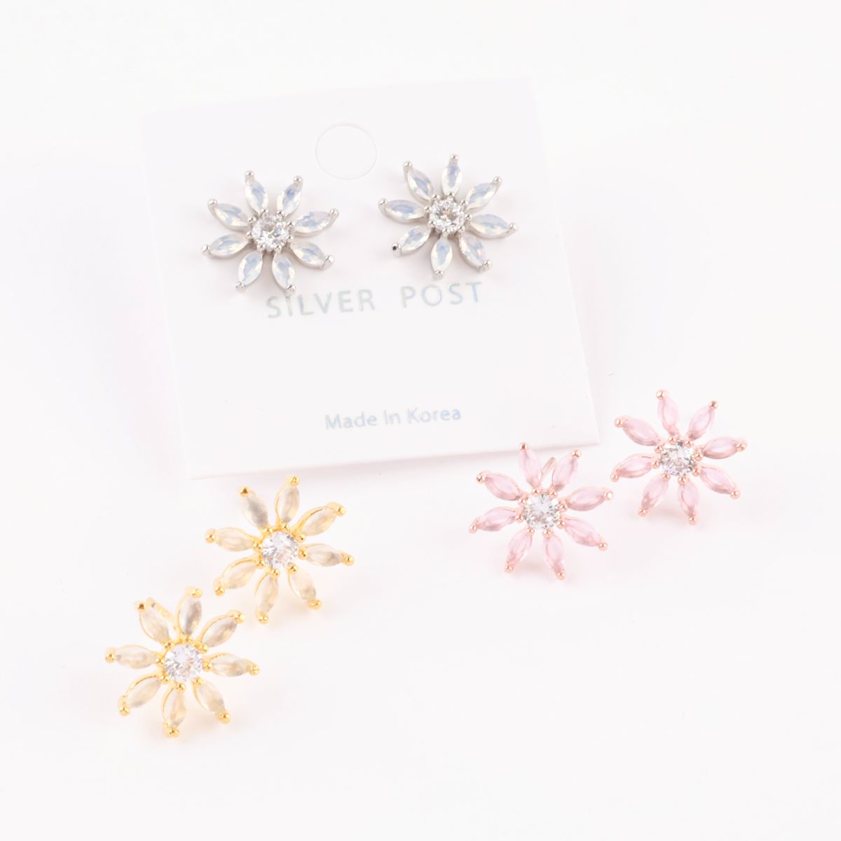 Three pairs of flower-shaped stud earrings in silver, gold, and pink, displayed on earring cards labeled "Silver Post – Made in Korea