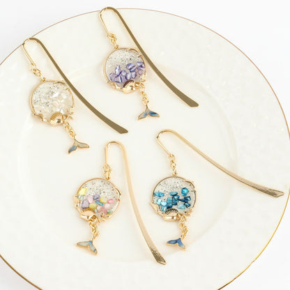 Pastel rainbow and ocean blue whale tail bookmarks placed in open novel showing shimmer detail