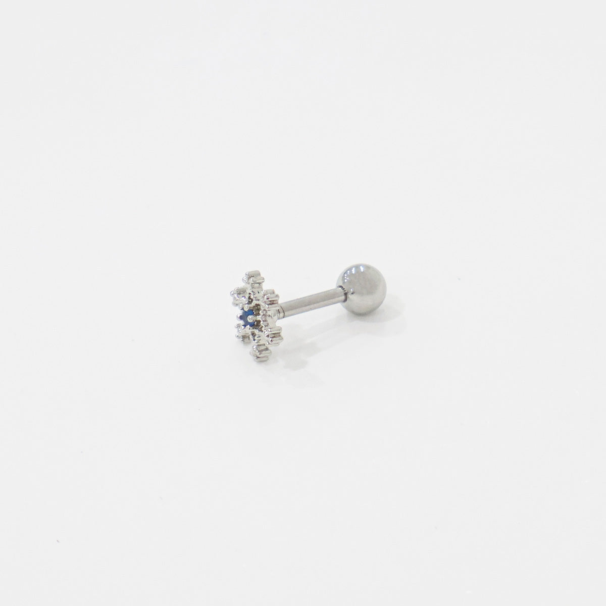Angled view of silver snowflake barbell earring placed on white surface.