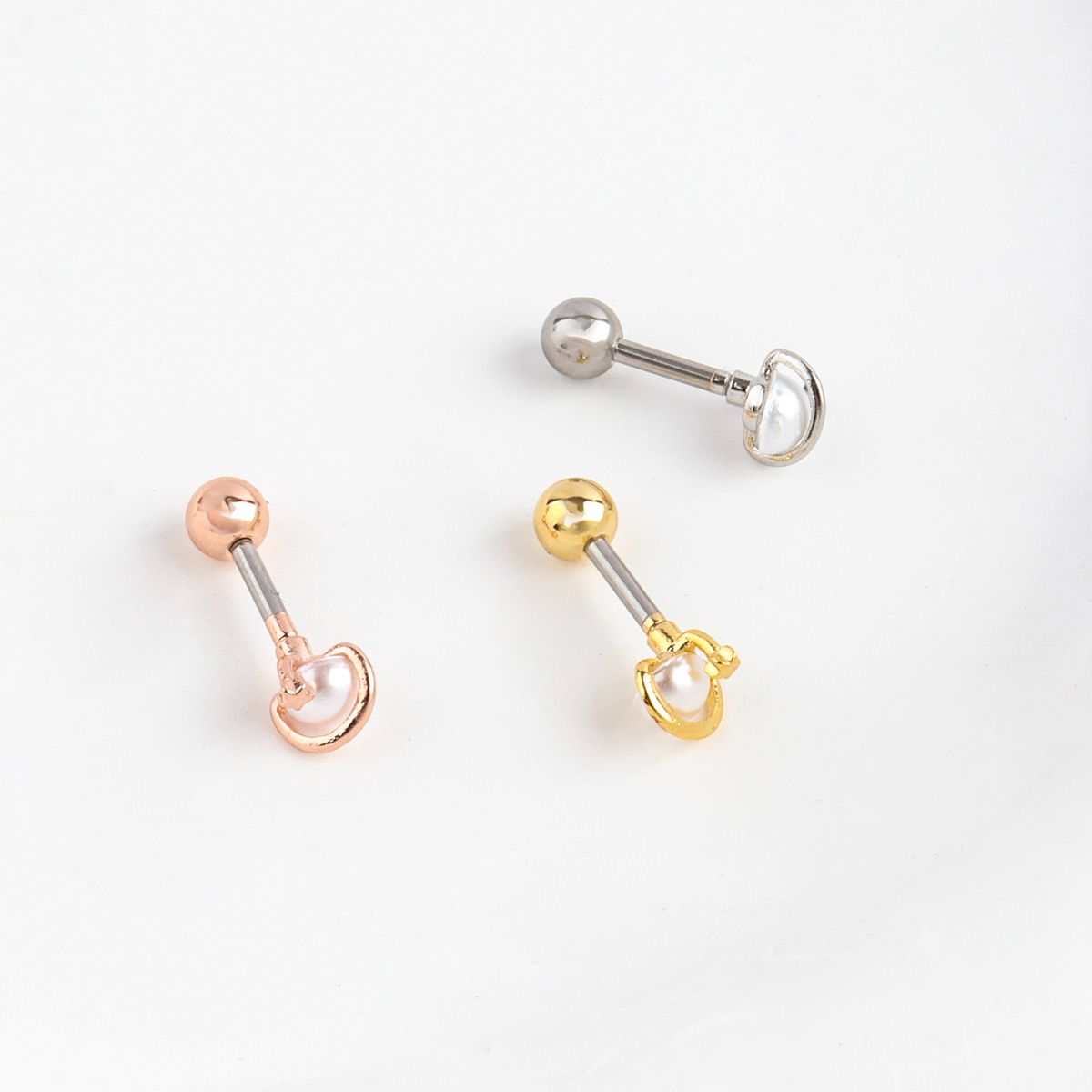 Flat lay of three Saturn planet pearl orbit barbell piercings in silver, gold, and rose gold with replaceable back balls