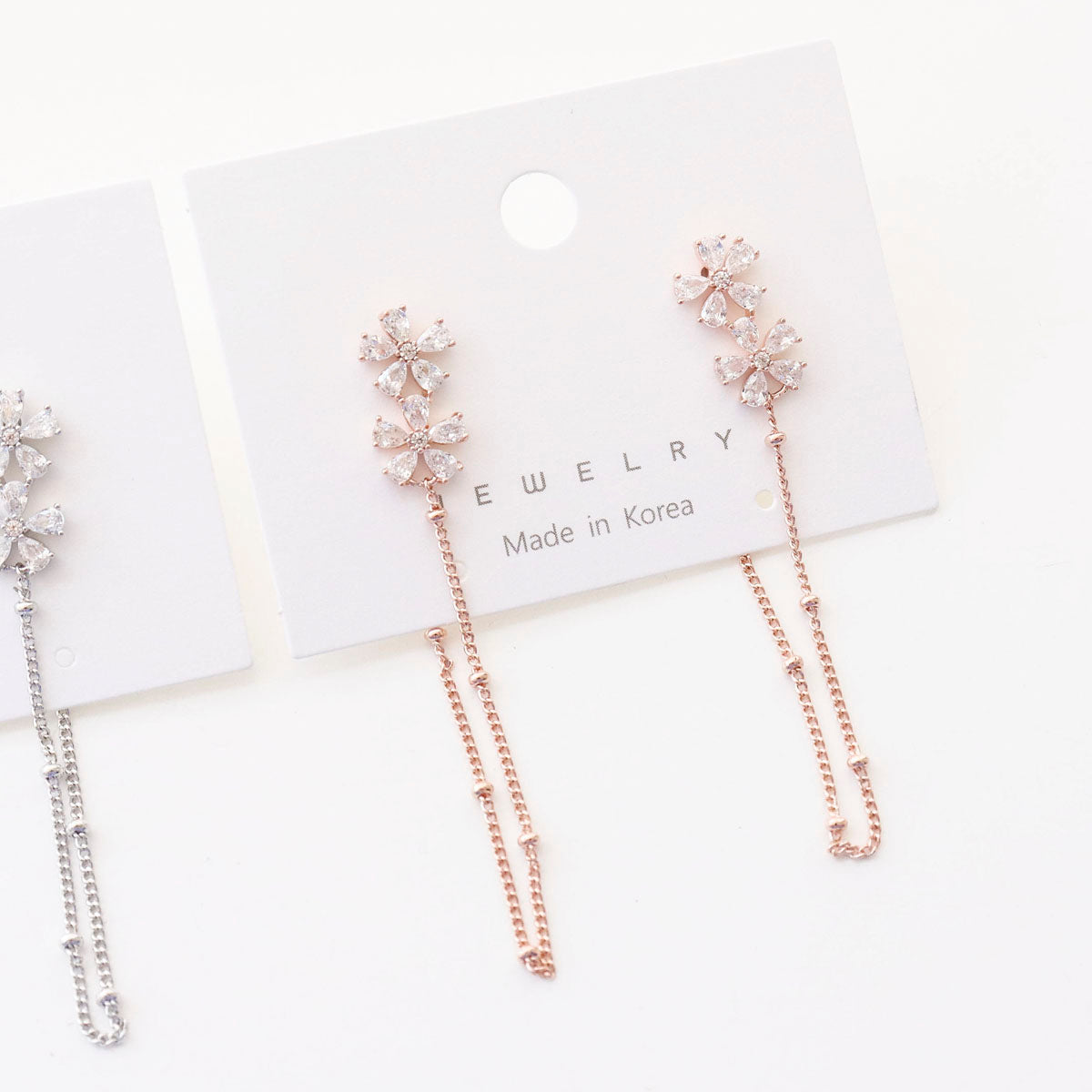 Close-up detail shot of rose gold flower CZ earrings with chain on card