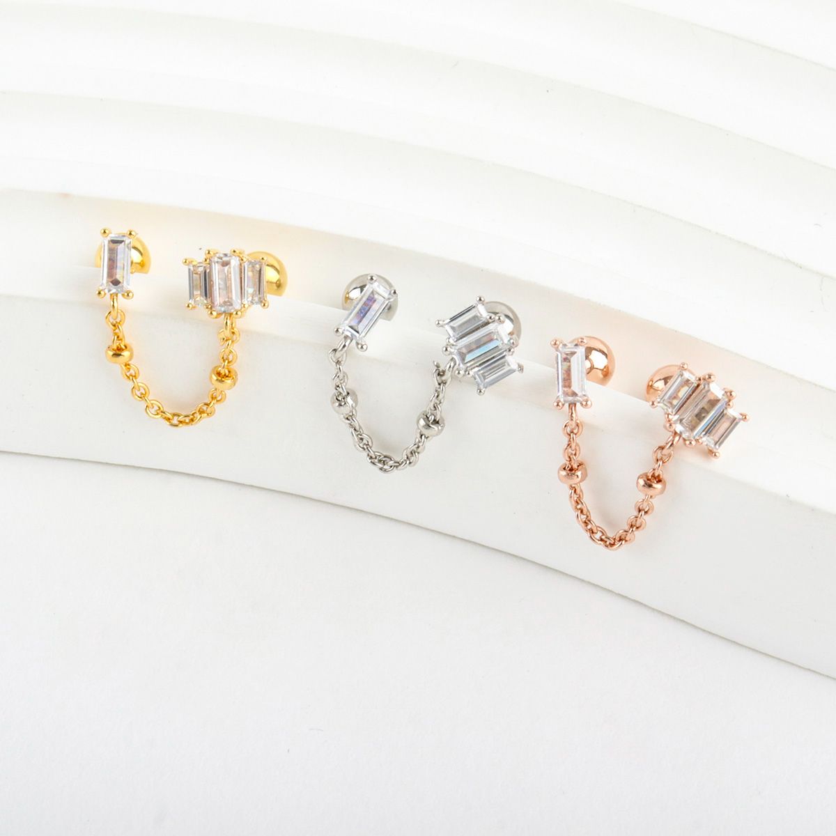 Top view of Baguette CZ Chain Double Stud Earrings in gold, silver, and rose gold, arranged neatly to display the sparkle of the stones and the curve of the chain.